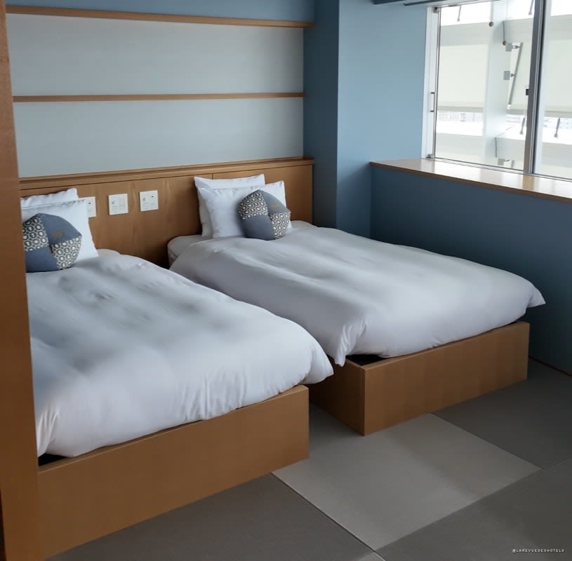 Lits jumeaux sur tatamis dans une chambre de l'OMO7 Osaka, banquette face à la baie vitrée