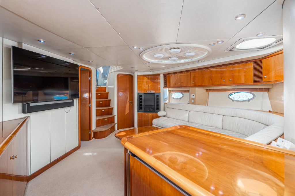 Sunseeker Predator 63 saloon interior — cream leather settee, cherry joinery, oval portholes, and stairs down to the cabins