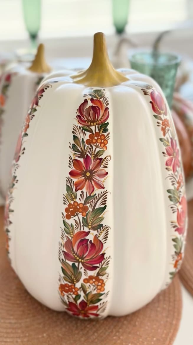 A white ceramic pumpkin with red and orange floral designs in the Petrykivka style.