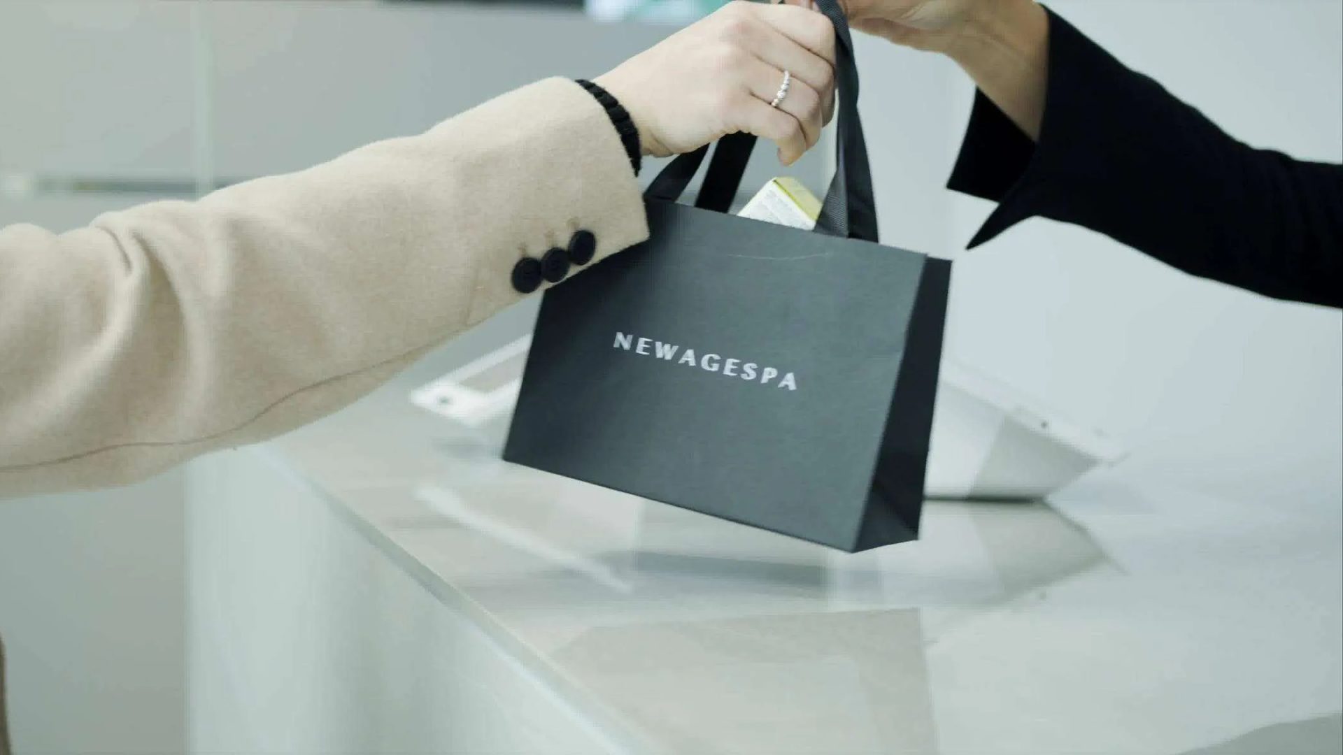 A branded New Age Spa bag being handed across a white reception counter