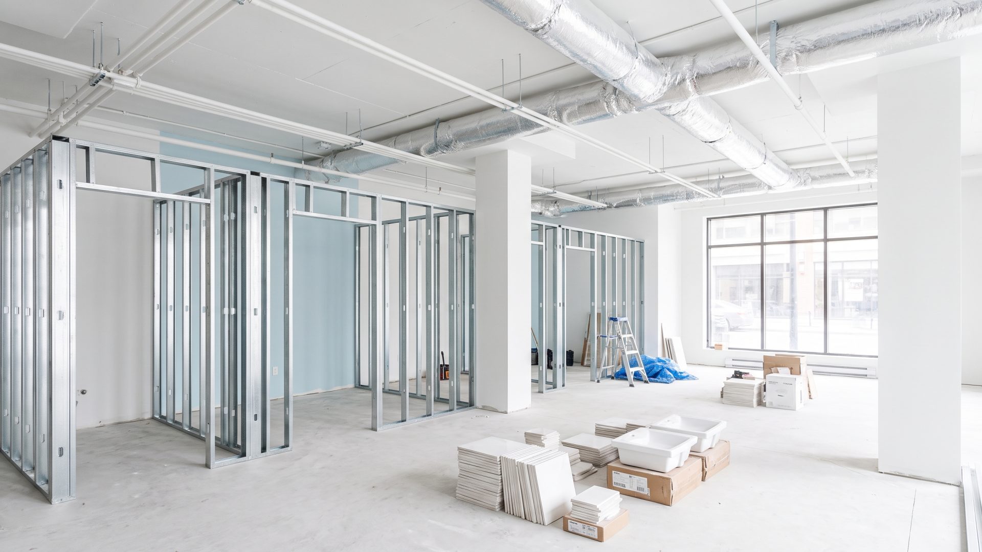 Une clinique en chantier : cloisons en montants métalliques délimitant plusieurs salles, gaines et conduits au plafond, matériaux empilés au sol