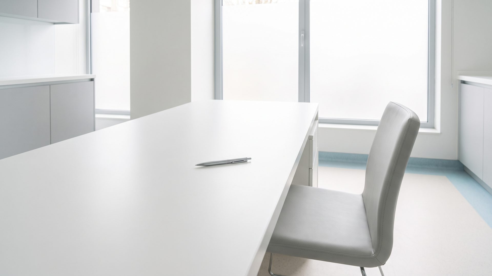 Un stylo seul sur un bureau blanc nu dans un local de clinique, une chaise vide recul&eacute;e