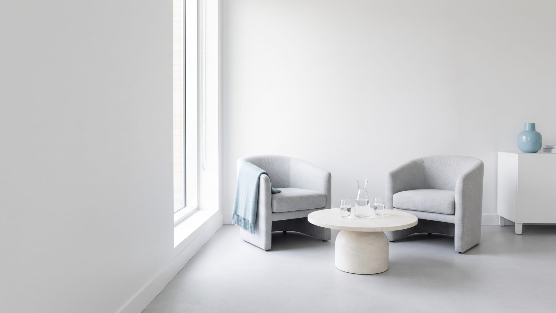 Two empty armchairs facing each other across a low table with a carafe of water, in a bright consultation corner