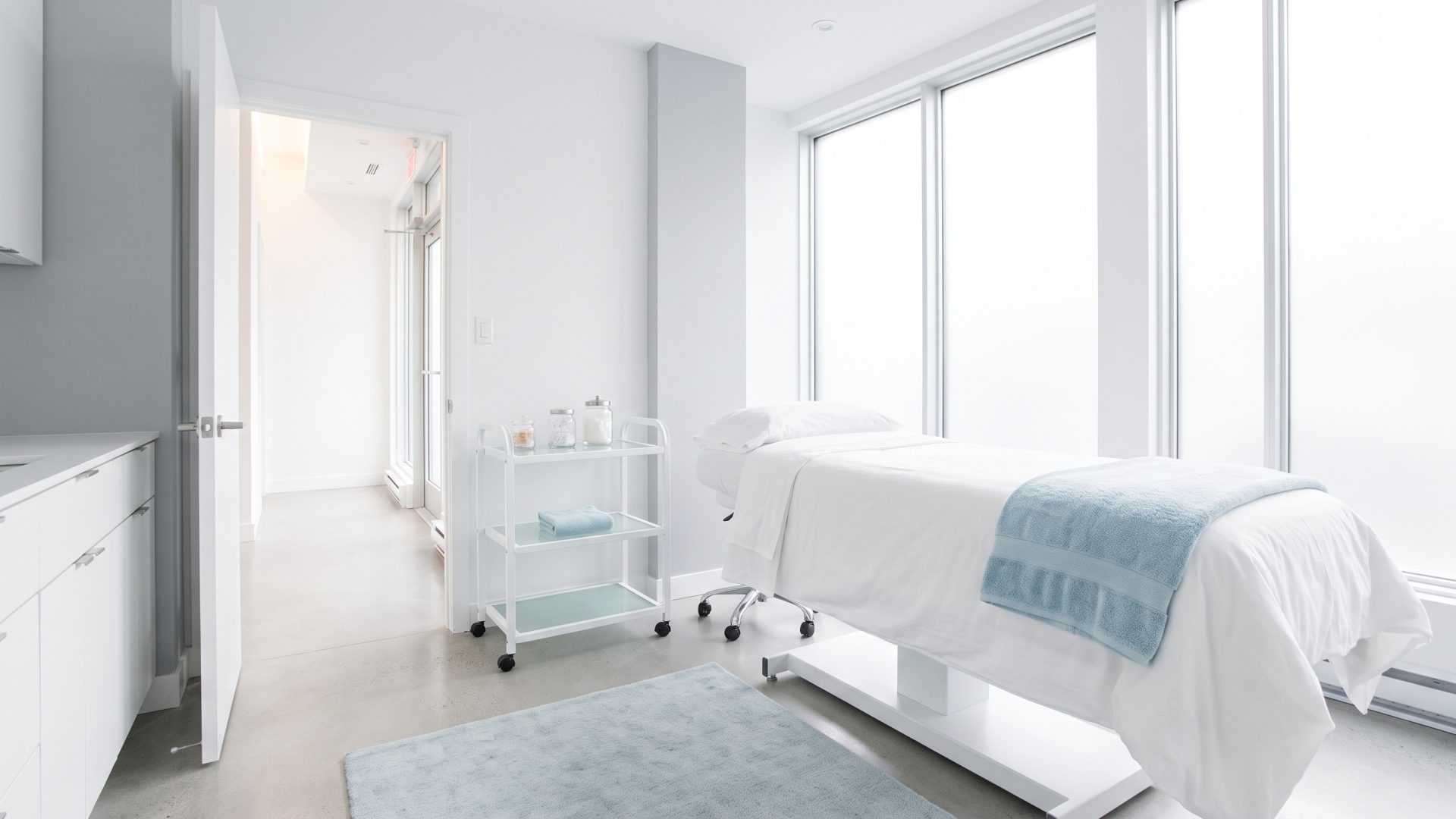 Une salle de traitement remise en ordre entre deux clientes, la porte ouverte sur un corridor lumineux