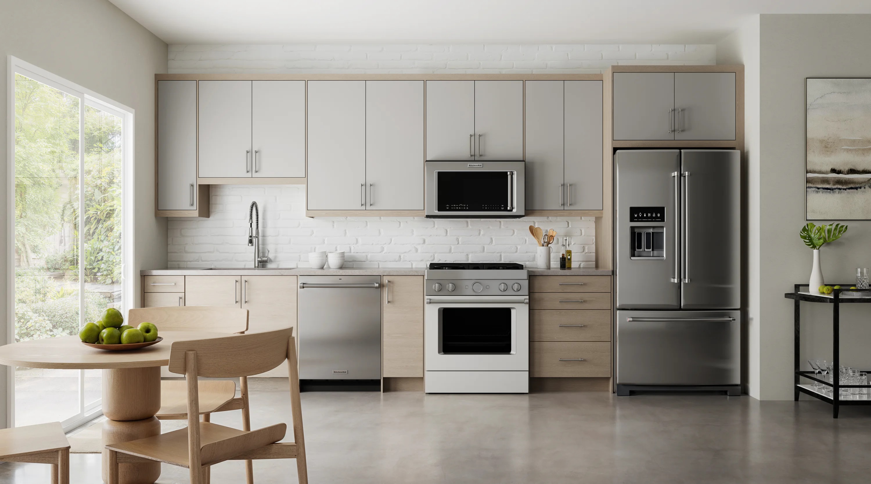Contemporary kitchen featuring dark black oak cabinetry with brass hardware, a round dining table surrounded by white-cushioned chairs, warm wood flooring, pendant lights over the island, and large windows and patio doors showcasing greenery outside.