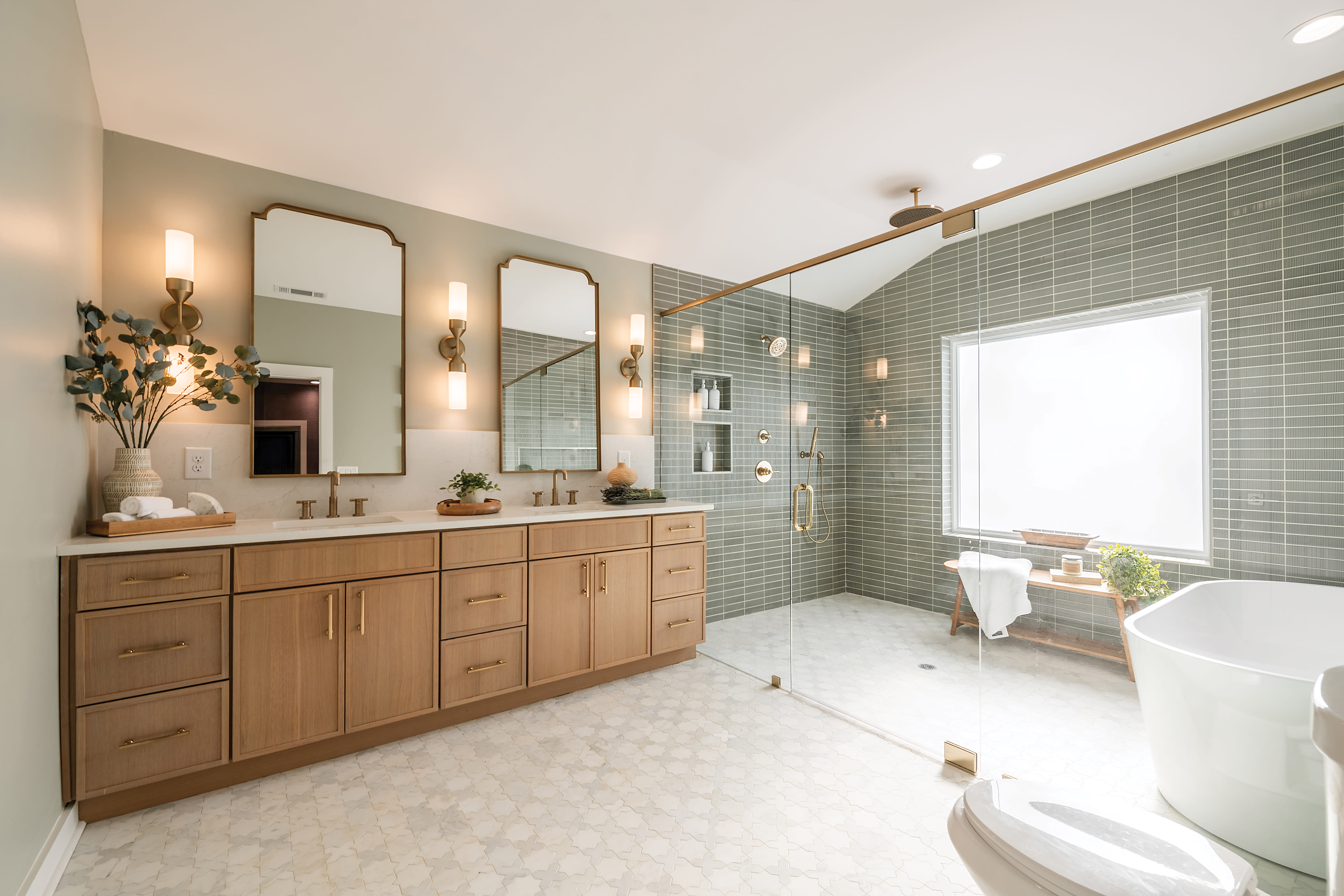 Bright bathroom with dual sinks, white mosaic Bedrosians tile flooring, and green shower subway tile with gold handles and trims