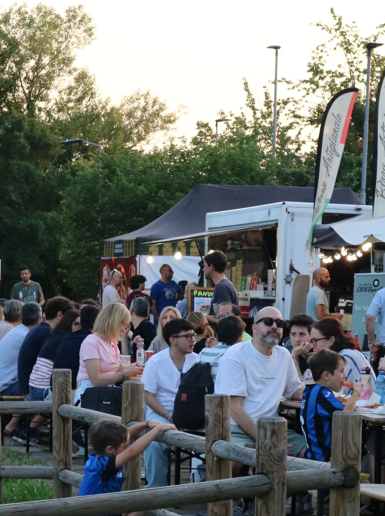 Persone sedute ai tavoli durante un evento serale con food truck