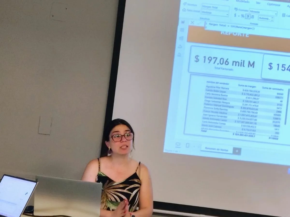 Paula Bria al frente de un aula, con un informe de ventas proyectado en la pantalla detrás
