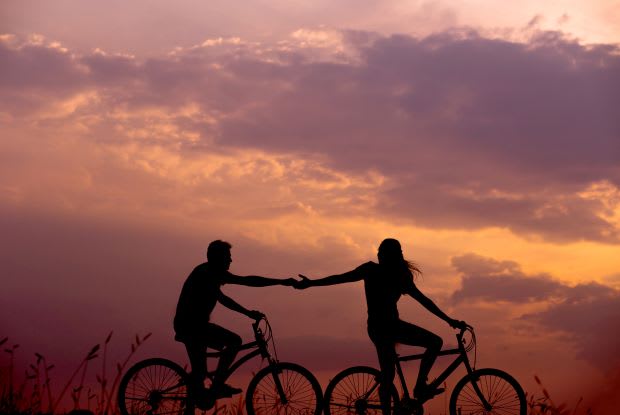 the silhouette of a couple holding hands while biking