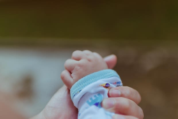 an adult’s hand holding an infant’s hand