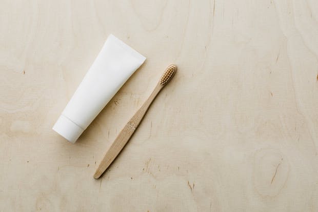 A plain white tube of cream with a small brush on a plain background