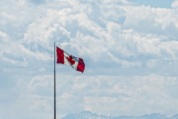 a Canadian flag waving with a light blue backdrop of the sky