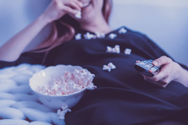 a person being inactive, eating popcorn while watching television