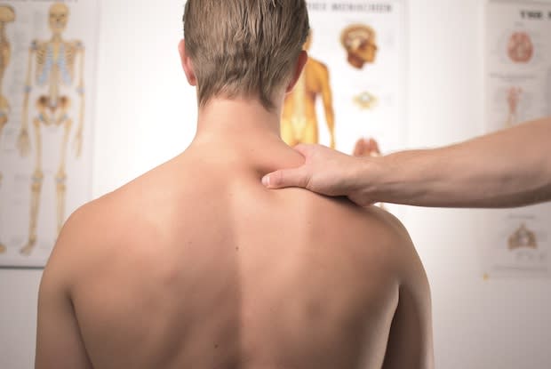 Bareback man sitting upright receiving massage to upper back