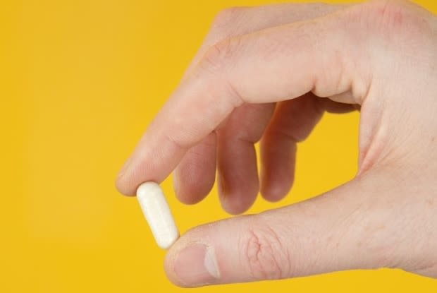 a hand holding a white pill on a yellow background