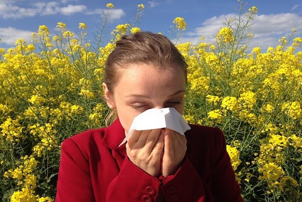 a woman blowing her nose in front of yellow plants