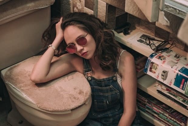 a girl sitting next to a closed toilet