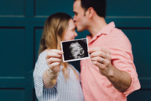 a man and woman holding a sonogram of a baby