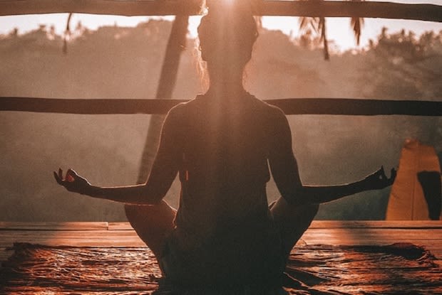 Silhouette of woman in seated yoga pose meditating as sun shines around her