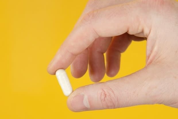 a hand holding a single pill on a yellow background