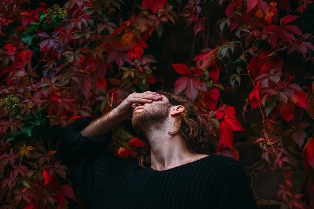 a man rubbing his eyes in front of a red plant