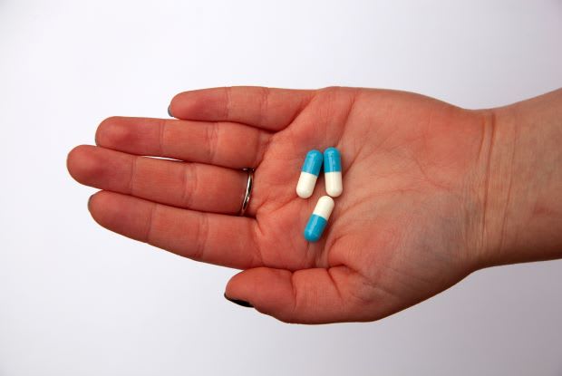 a hand holding three blue and white pills