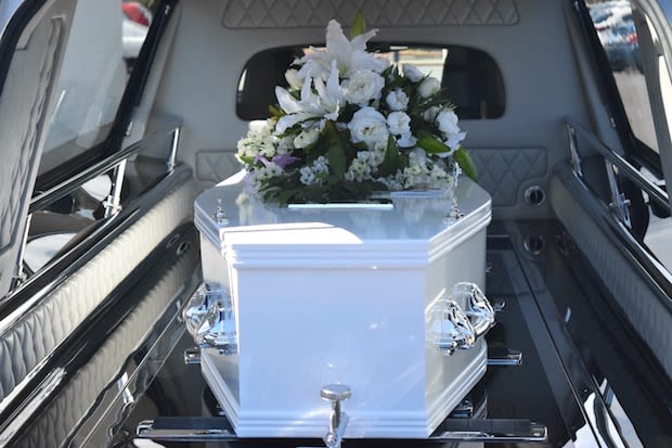 A white coffin with flowers on top in the back of a hearse