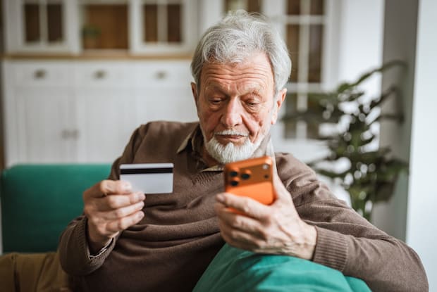 an elderly man making an online purchase with his credit card and mobile phone