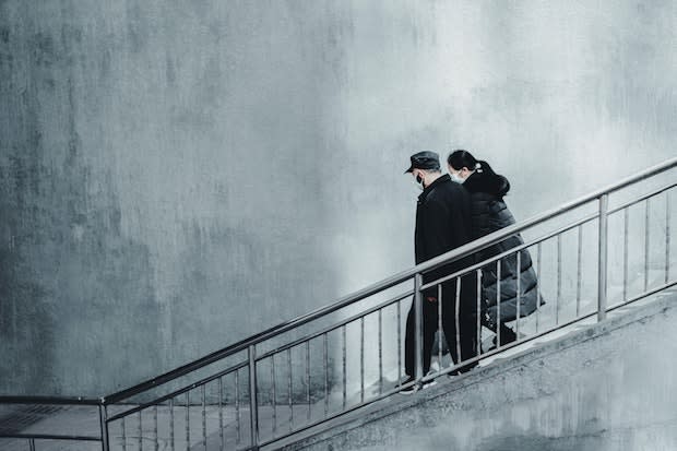 two people wearing masks walk down a staircase