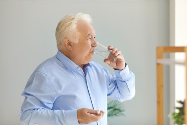 An elderly man taking medication with a glass of water