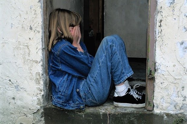 a younger child sitting in a doorway, covering her face