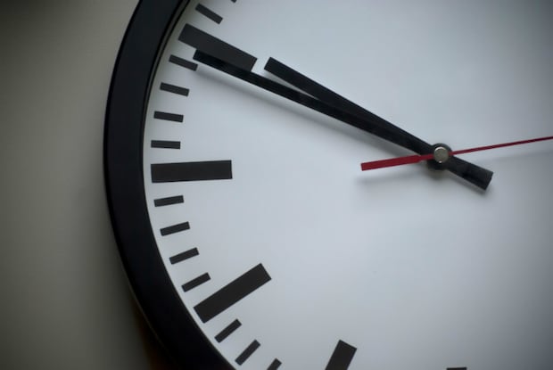 Part of a clock is shown resting against a gray wall.