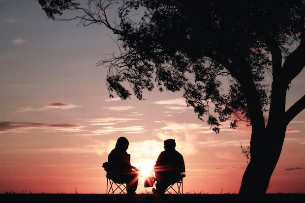 two people sitting in chairs as the sun sets