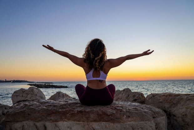 a woman sitting cross-legged on a rock near the ocean