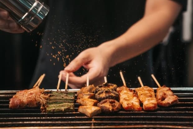 a street food vendor seasoning skewers