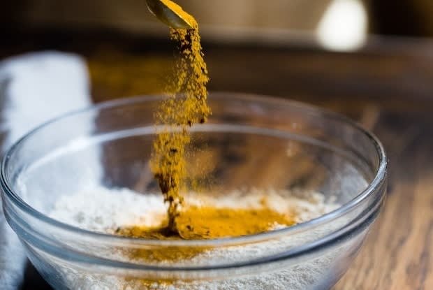 a hand sifting through turmeric powder with a spoon