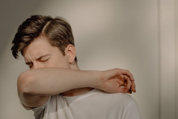 A young man coughing into his elbow