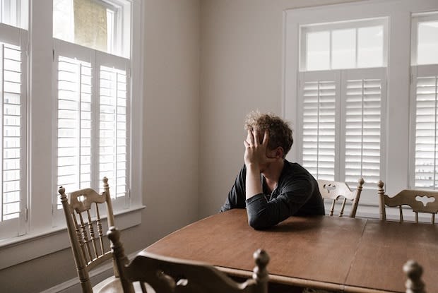 man sitting at wooden table holding head in hand