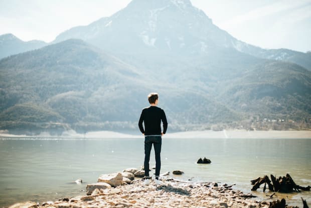 A man looks at mountains from across a body of water.