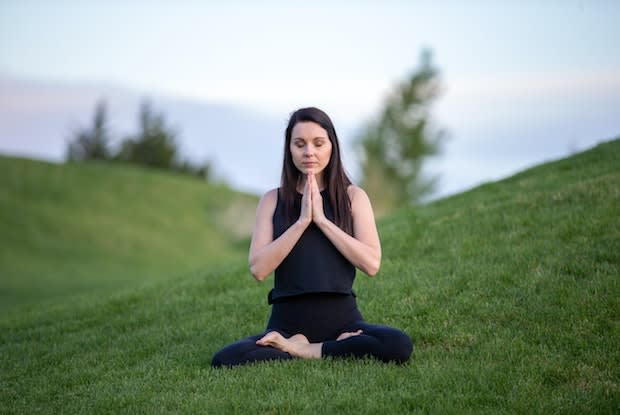 a woman meditating on a grassy hill