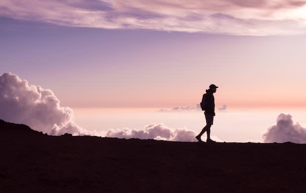 a person walking on a plateau with a backdrop of a purple sky