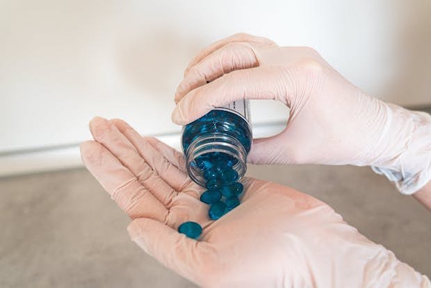 Pouring blue pills out of a bottle into a gloved hand