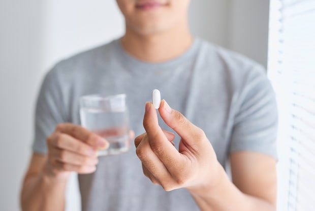 a man holding a white pill and a glass of water