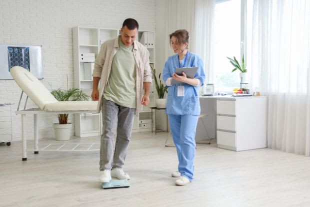 A man at a doctor’s office stepping on a weighing scale