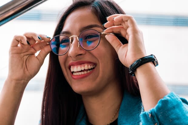 a smiling woman holding her glasses