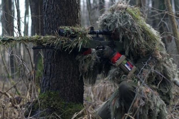 A soldier holding a gun camouflaged against the forest