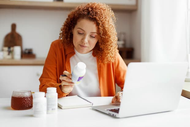A woman sitting in front of her laptop and looking at a prescription bottle