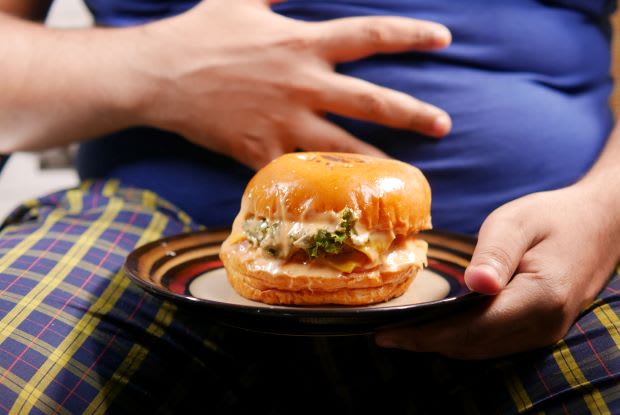 a person holding their stomach with one hand and a greasy burger with the other