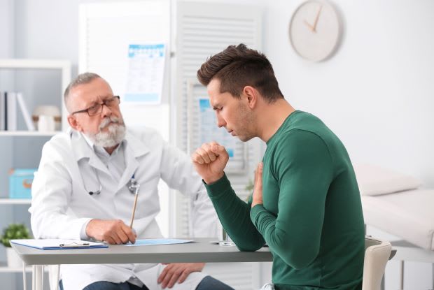 a man holding his lung area and coughing while at a doctor’s appointment