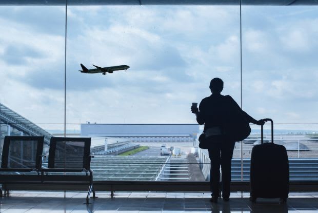 Person at airport window holding a suitcase